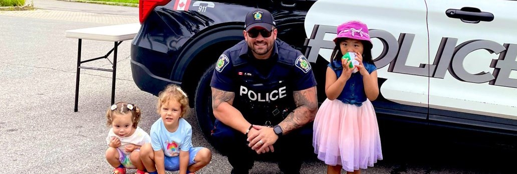 An officer in front of a cruiser with some kids