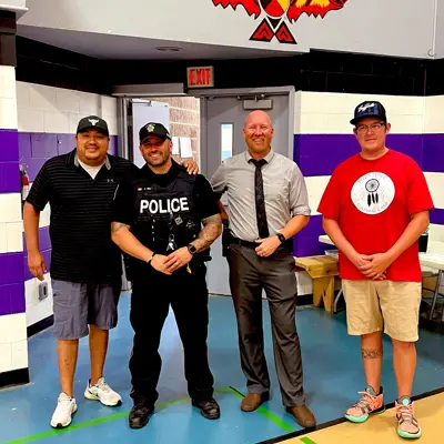 A police officer posing for a photo with 3 community members in a gymnasium