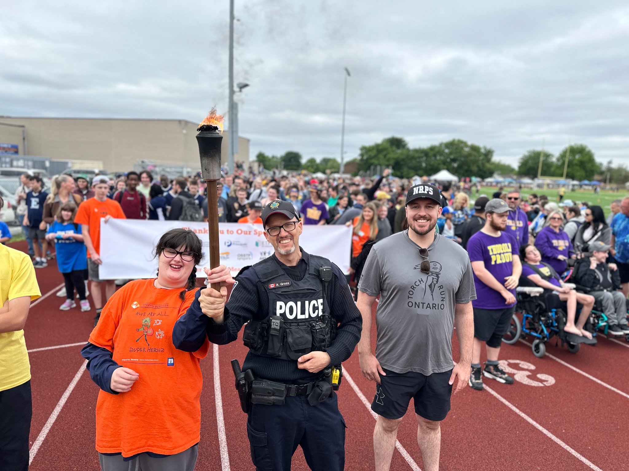 An officer with two other people holding a torch in front of a banner and a crowd of people