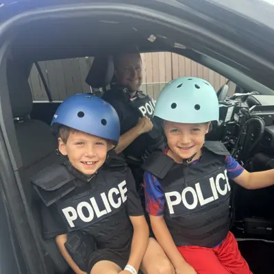Two kids sitting in a police cruiser with an officer. 