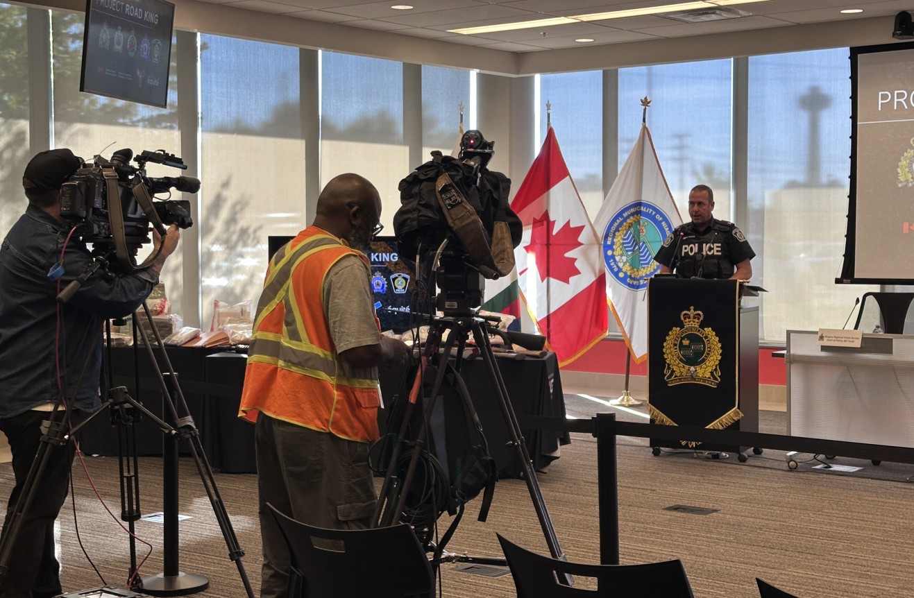 Someone speaking at a podium with two television cameras pointed towards them